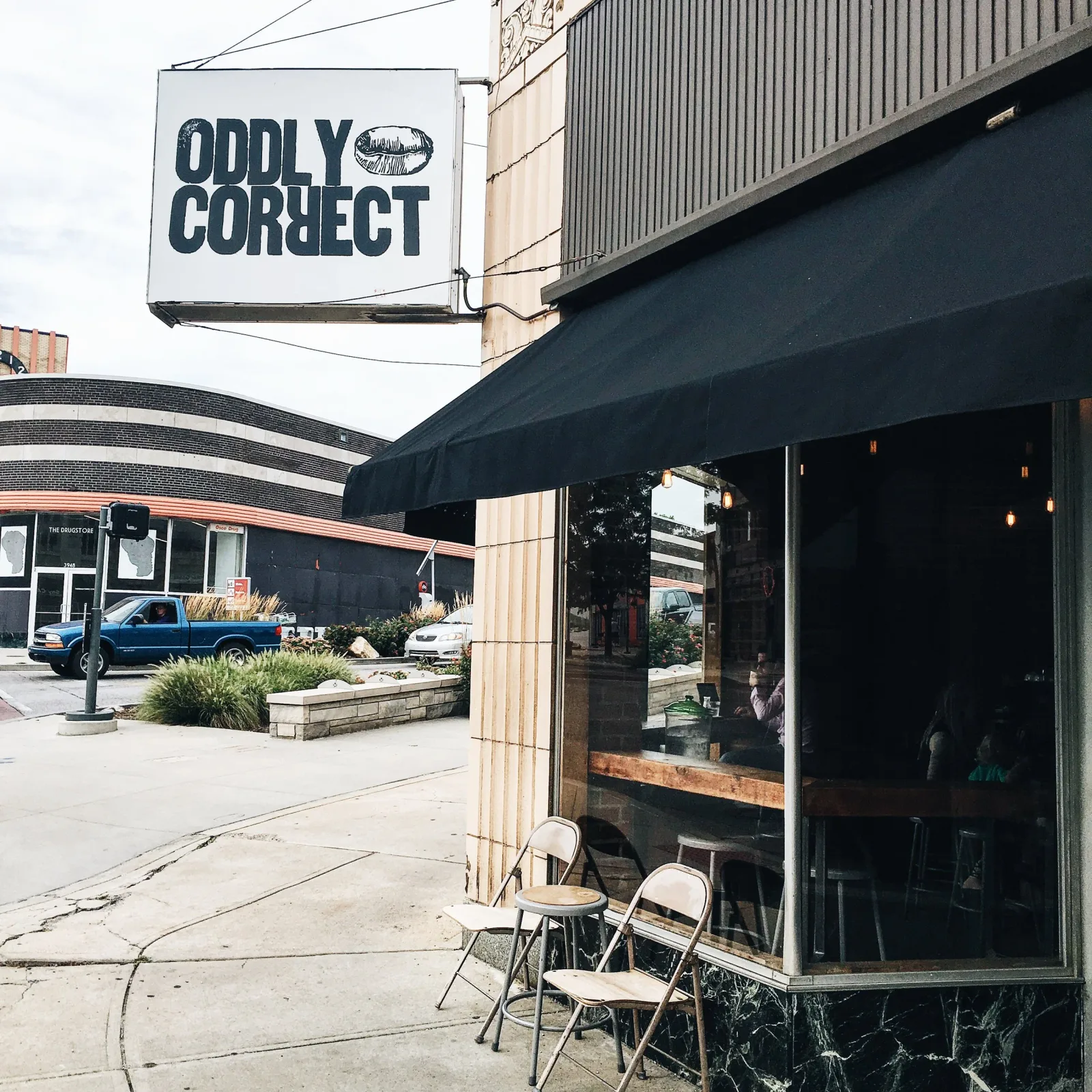 storefront with "oddly correct" sign, black awning, outdoor seating, urban street., oddly correct coffee bar, kansas city