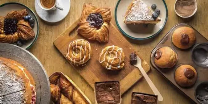 assorted baked goods and pastries arranged on wooden surface with coffee cups., old madras baking company (adayar), chennai