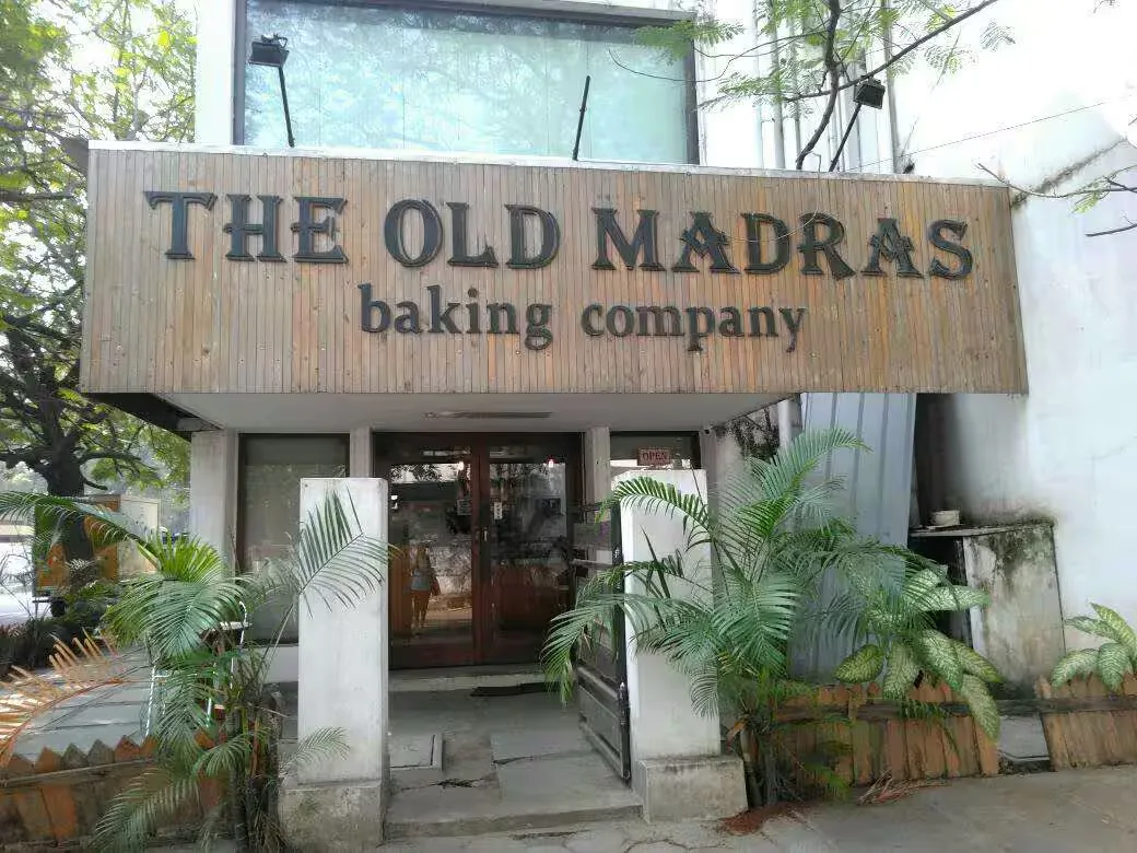 wooden storefront signage for "the old madras baking company" with potted plants., old madras baking company (adayar), chenna