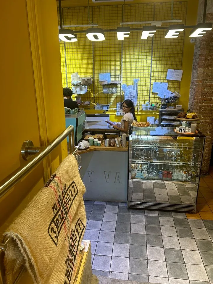yellow coffee shop interior with staff behind counter and bright signage., onyva coffee sant gervasi | cafe de especialidad |