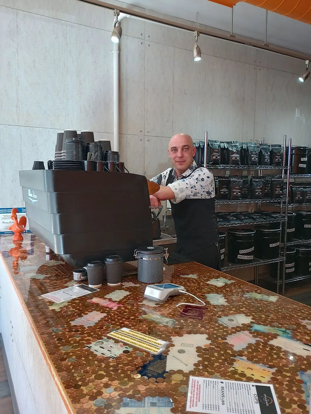 man stands at counter with large coffee dispenser and coin-embedded surface., opulence coffee, ottawa
