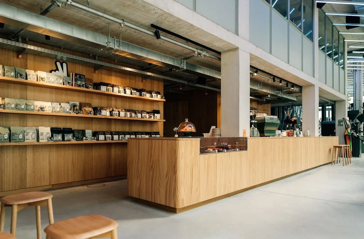 modern wooden café counter with shelved product displays and copper dome service bell., pacandé kaffeerösterei kg, munich
