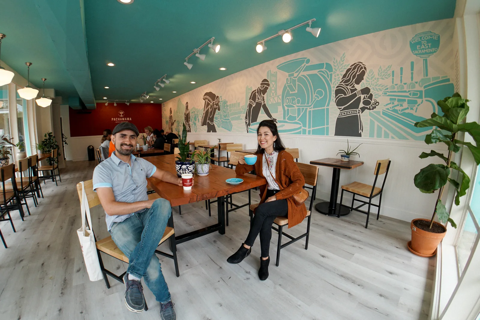 two people seated at wooden table in modern turquoise and white cafe interior., pachamama coffee, sacramento