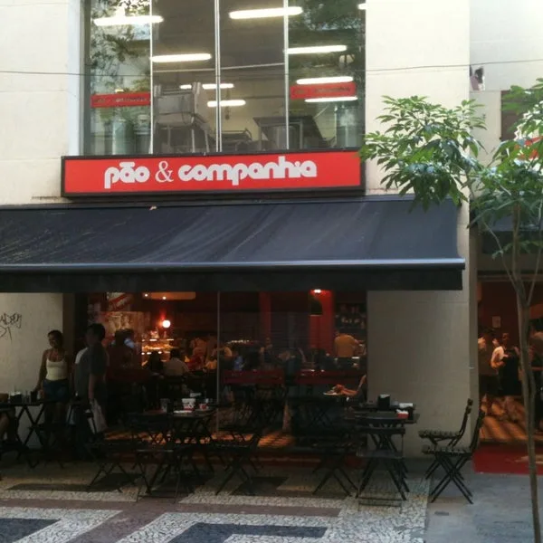 red and black storefront "pão & companhia" with outdoor seating and pedestrians., pão & companhia, rio de janeiro