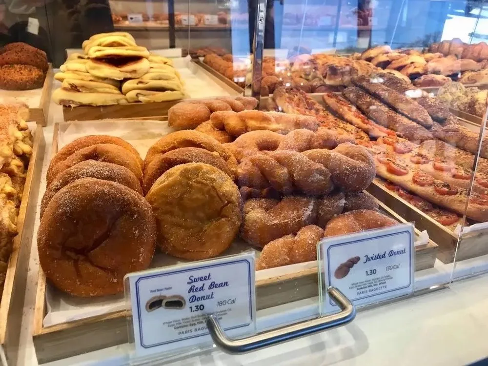 bakery display case with donuts, pastries, and yellow bananas behind glass., paris baguette, houston