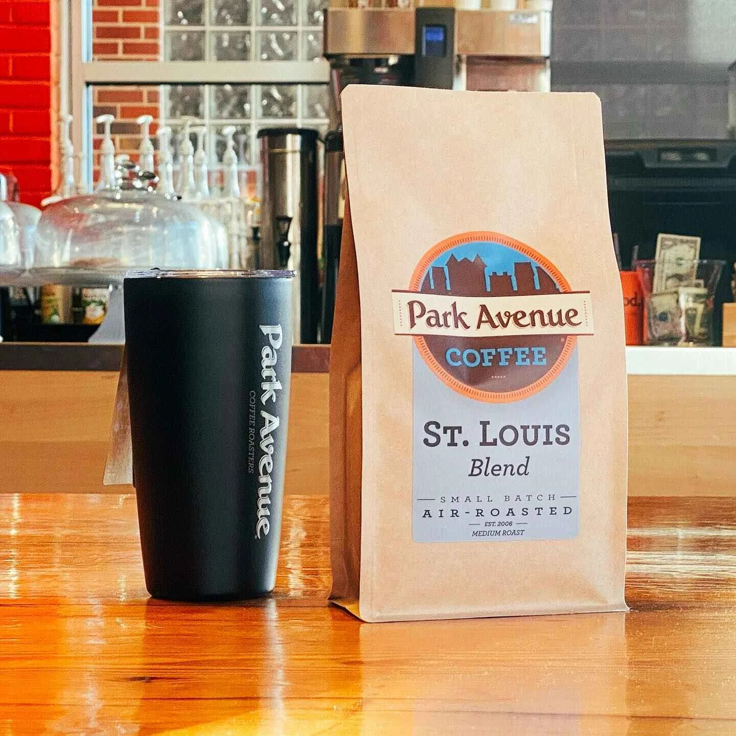 park avenue coffee st. louis blend bag next to black tumbler on wooden counter., park avenue coffee roasters, st. louis