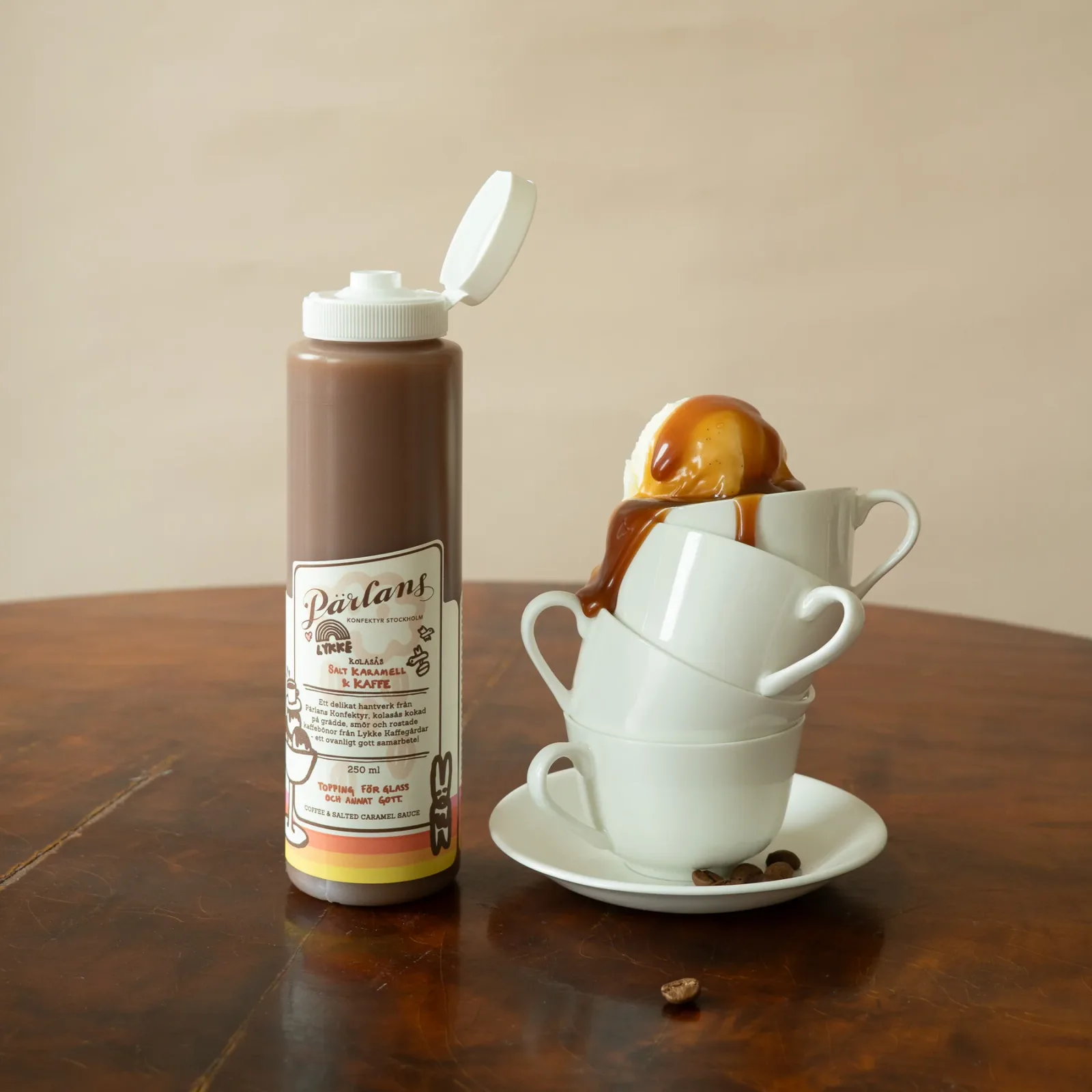 parlans salted caramel sauce bottle beside stacked white cups with caramel drizzle., pärlans konfektyr, stockholm