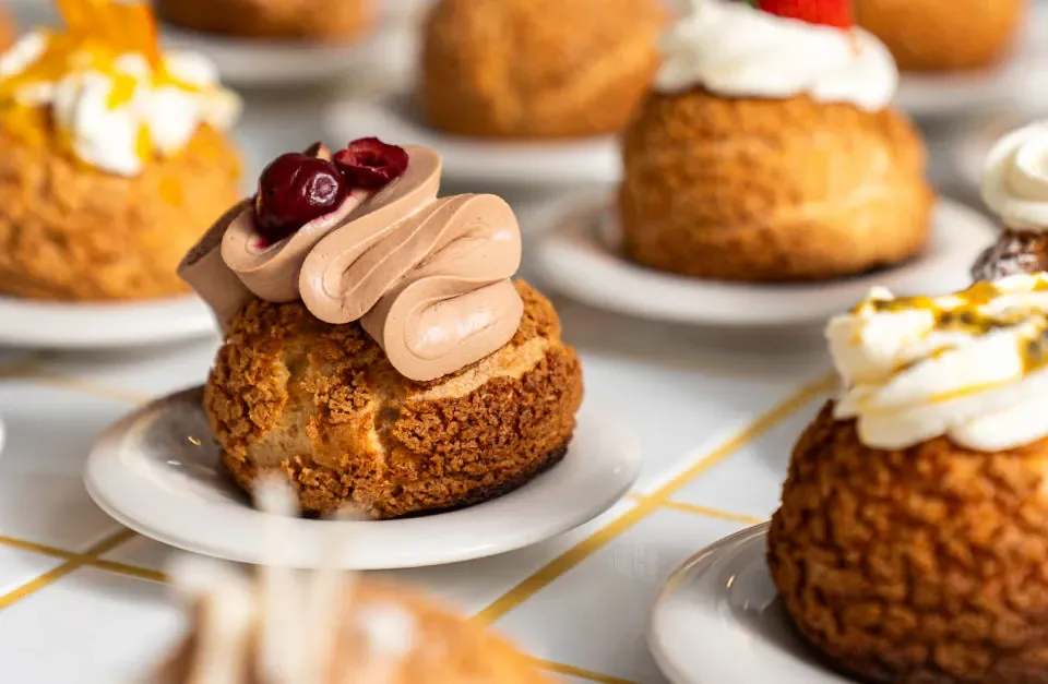 gourmet pastries with chocolate frosting and cherry garnish on white plates., paska.l choux p-berg, berlin