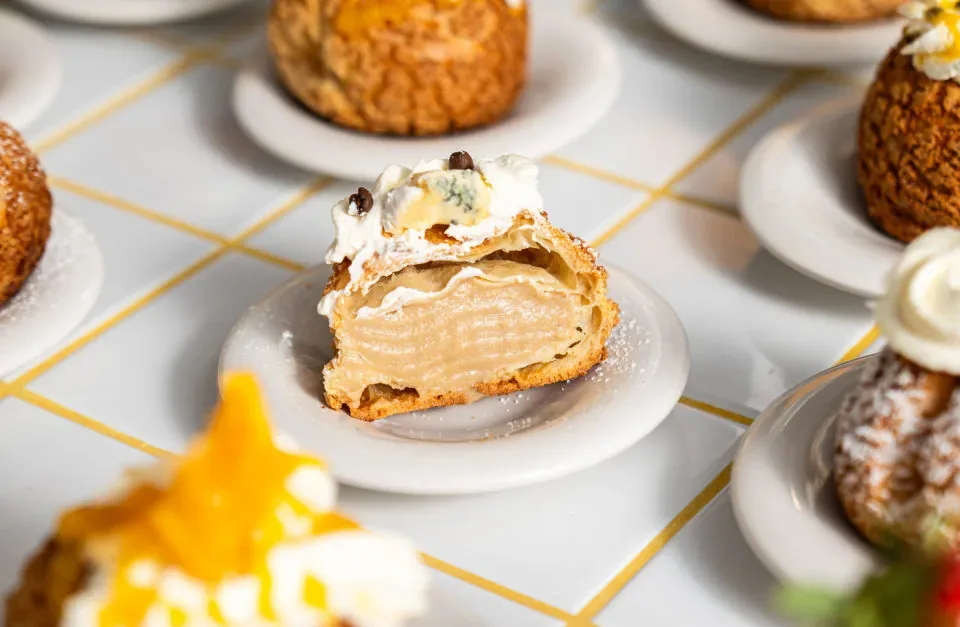 elegant pastry profiteroles with cream filling displayed on white plates with gold trim., paska.l choux p-berg, berlin