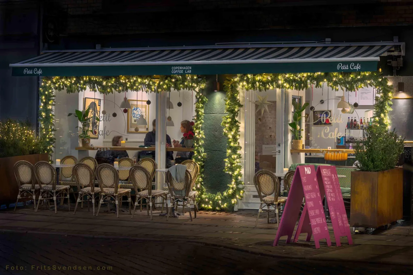 illuminated copenhagen coffee café storefront decorated with festive garland and warm lights., petit cafe, copenhagen