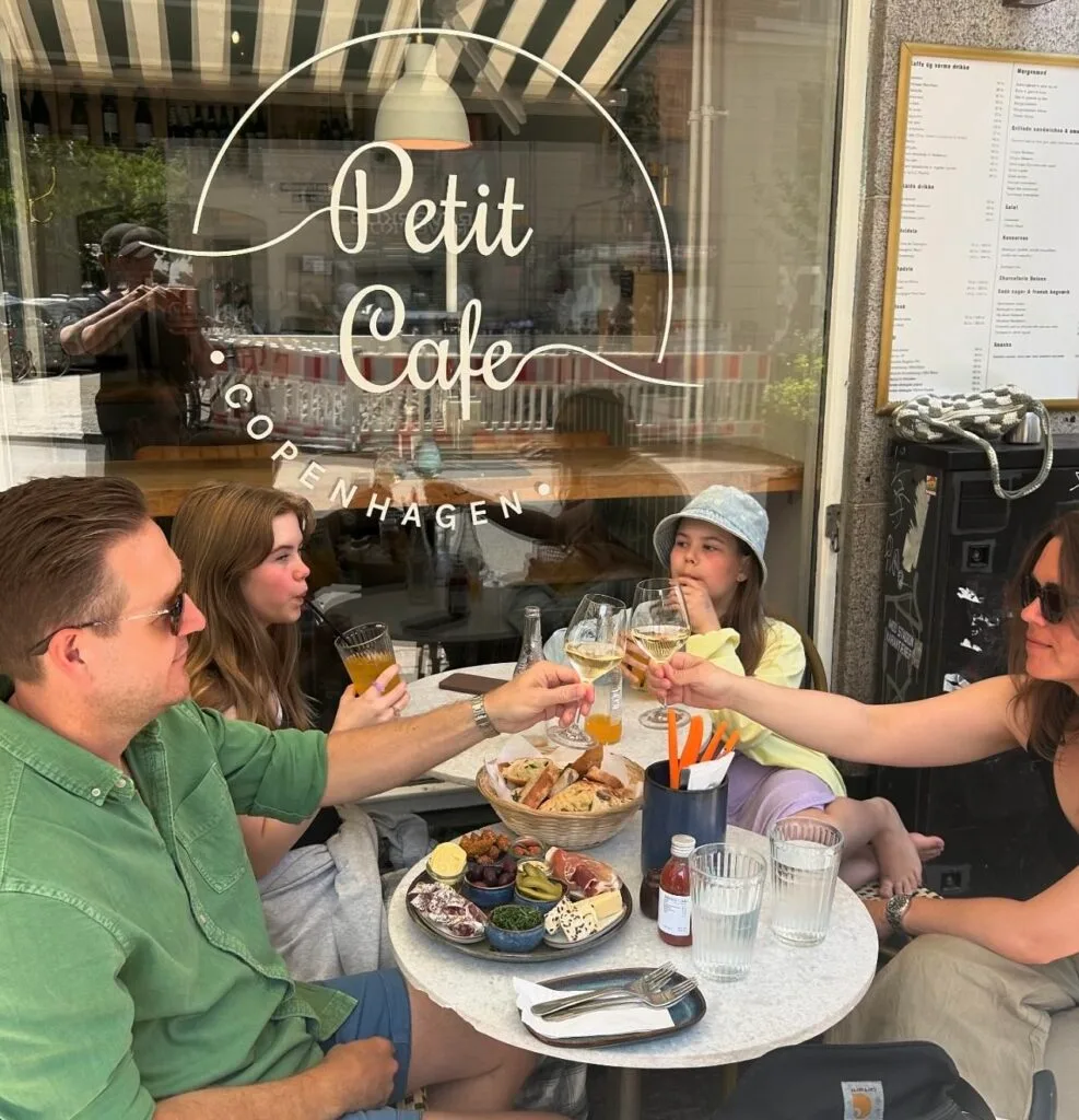 four people dining outdoors at petit cafe copenhagen, toasting with glasses., petit cafe, copenhagen