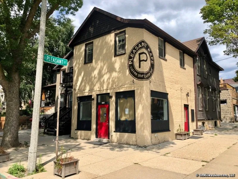 corner building with cream brick facade, red doors, pleasant street sign visible., pilcrow coffee, milwaukee