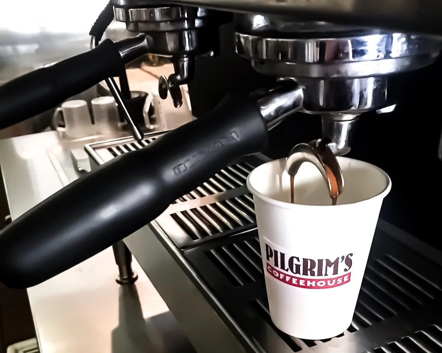 espresso machine dispensing dark coffee into pilgrim's coffeehouse branded cup., pilgrim's coffeehouse, fullerton