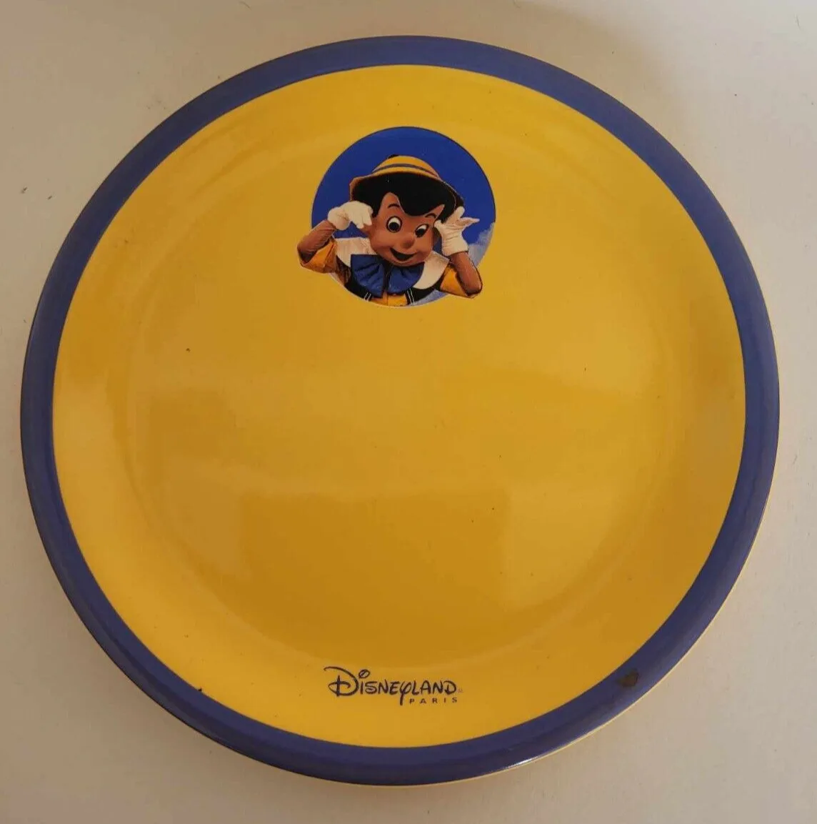 yellow and blue plate featuring paddington bear character from disneyland paris., pinocchio, paris