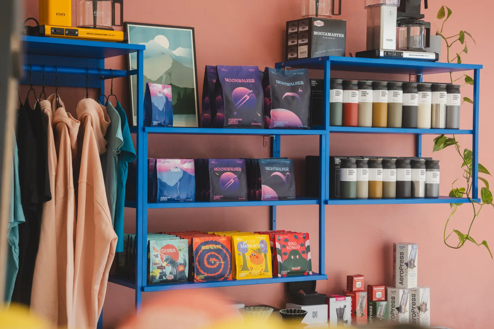 blue shelving unit displaying coffee equipment, books, and merchandise against pink wall., playground coffee st. pauli, hambu