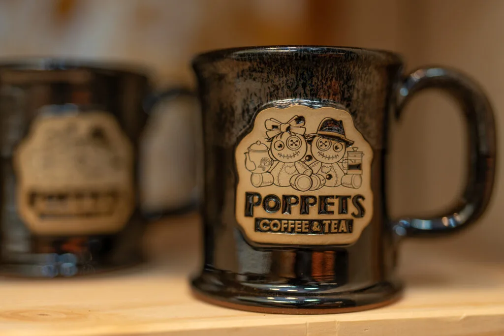 dark ceramic mug with "poppets coffee & tea" logo featuring decorative scarecrow characters., poppet's coffee, dayton