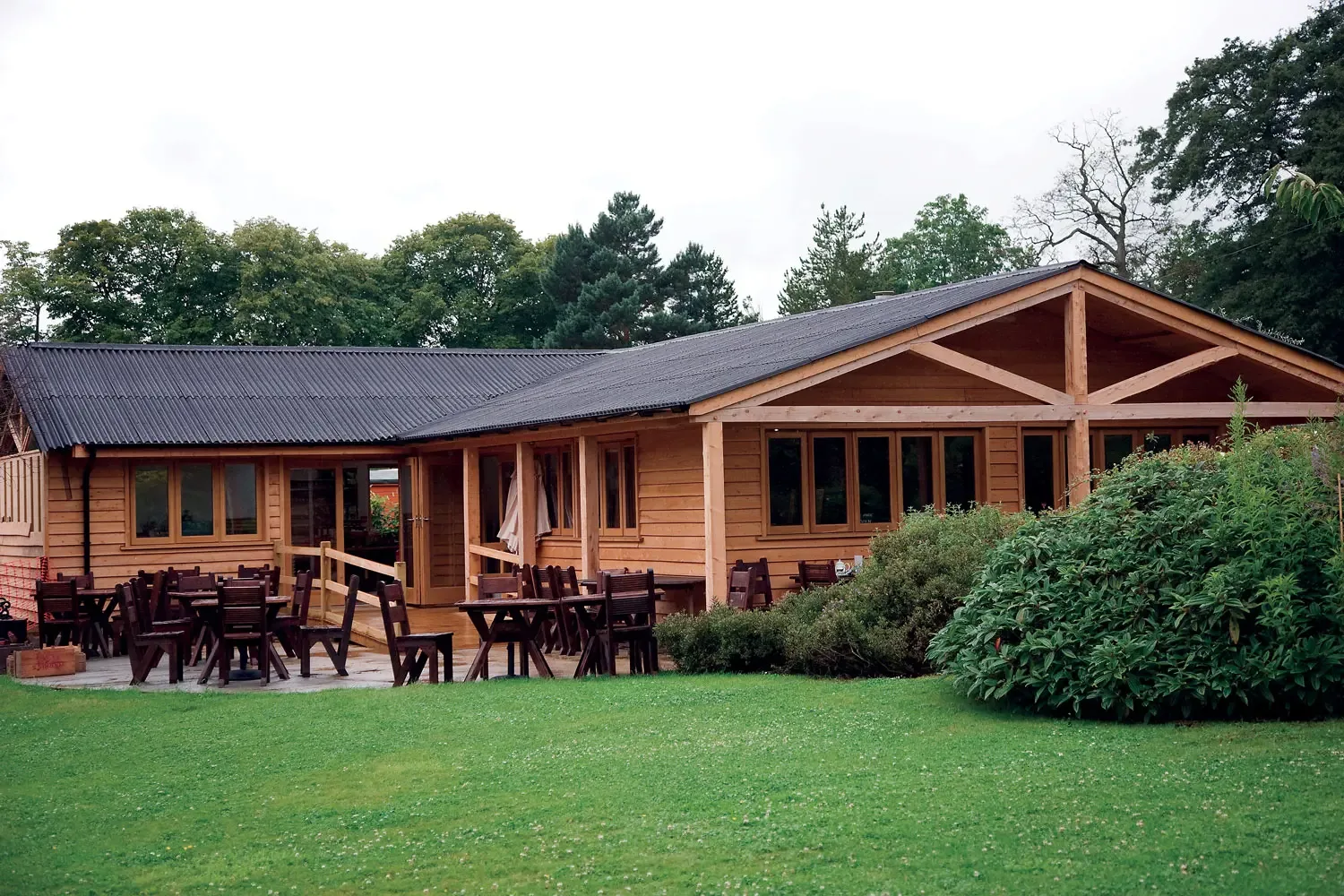 modern wooden lodge with dark roof, patio seating, manicured lawn, surrounding trees., quarr abbey, ryde