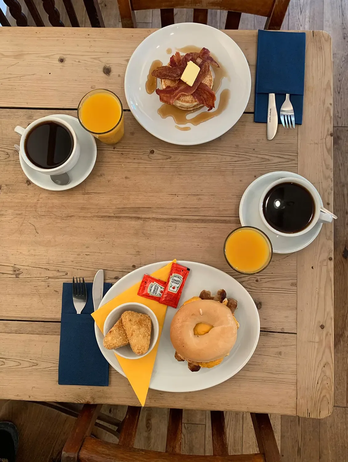 two place settings with pancakes, bacon, donuts, coffee, and orange juice on wooden table., quarr abbey, ryde
