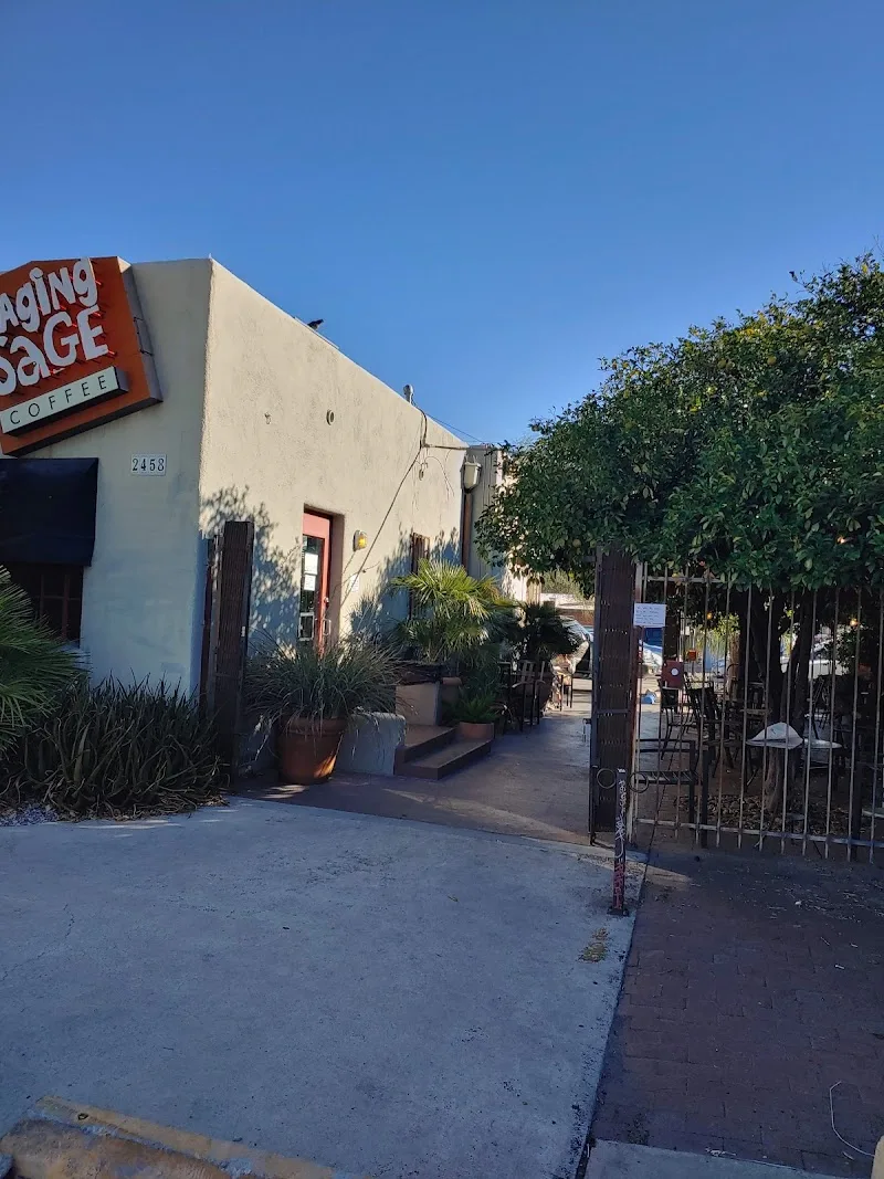 coffee shop storefront with cream-colored building and red signage, gated patio seating area., raging sage coffee roasters, a