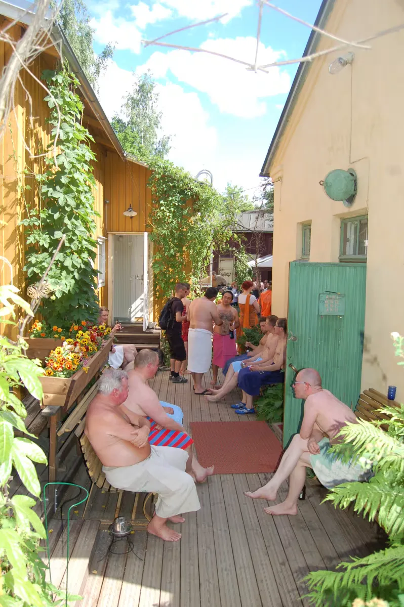 sauna courtyard gathering with shirtless men and clothed visitors on wooden deck., rajaportti sauna, tampere