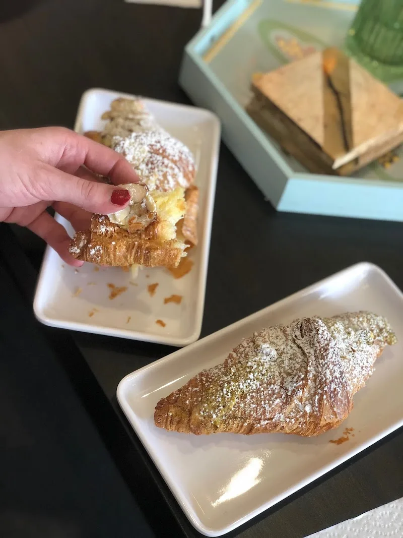 hand holding powdered pastry with cream filling above white plate., rapalo coffee roasters, hurst