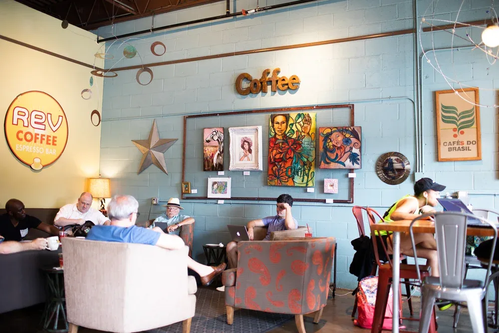 coffee shop interior with customers seated, colorful artwork displayed on walls., rev coffee, atlanta
