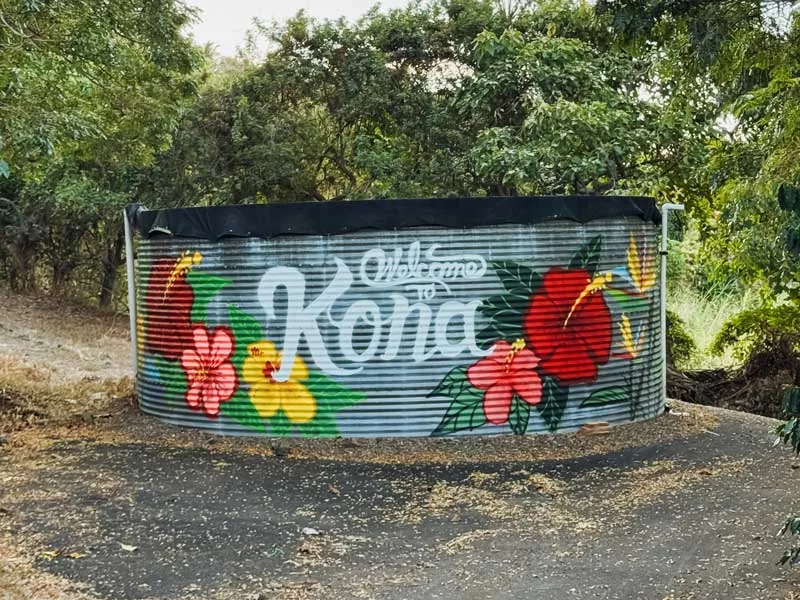 colorful painted water tank with flowers and "kona" text in rural setting., rising kona coffee farm tours, kailua-kona