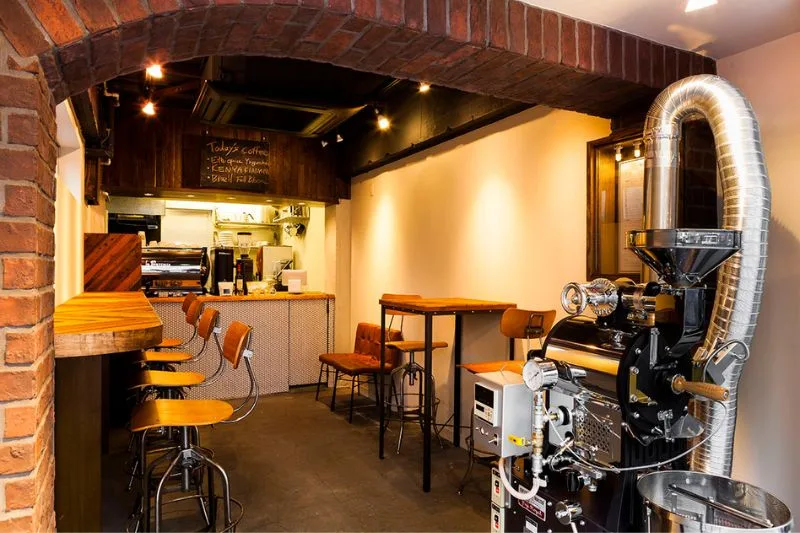 specialty coffee roastery with roaster machine, counter seating, and brick archway., roar coffeehouse & roastery, tokyo