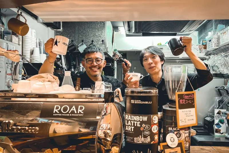 two coffee shop workers cheerfully holding cups and pots behind counter., roar coffeehouse & roastery, tokyo