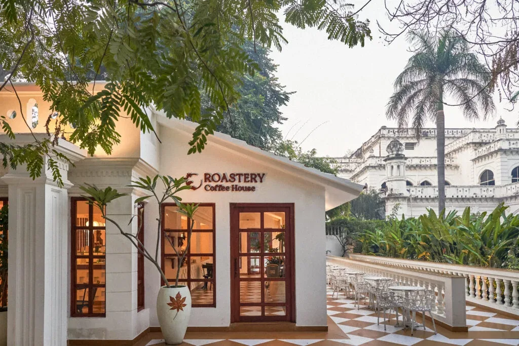 white coffee house with brown doors nestled among tropical gardens and colonial architecture., roastery coffee house | jahang