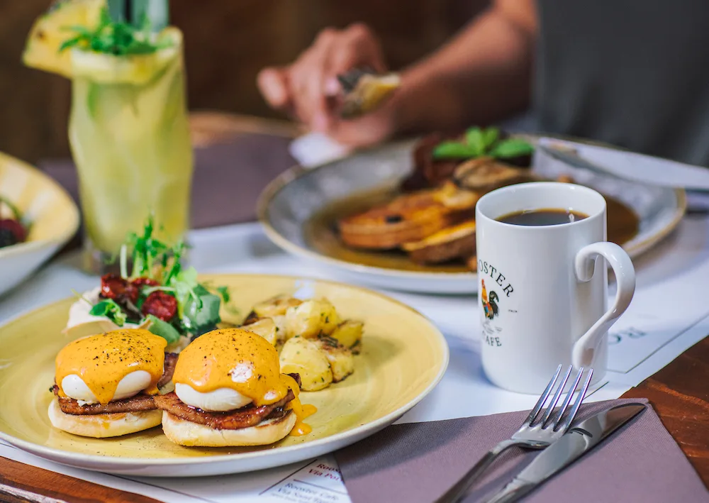 eggs benedict with hollandaise sauce, hash browns, coffee mug, and refreshing citrus beverage on dining table., rooster cafe 