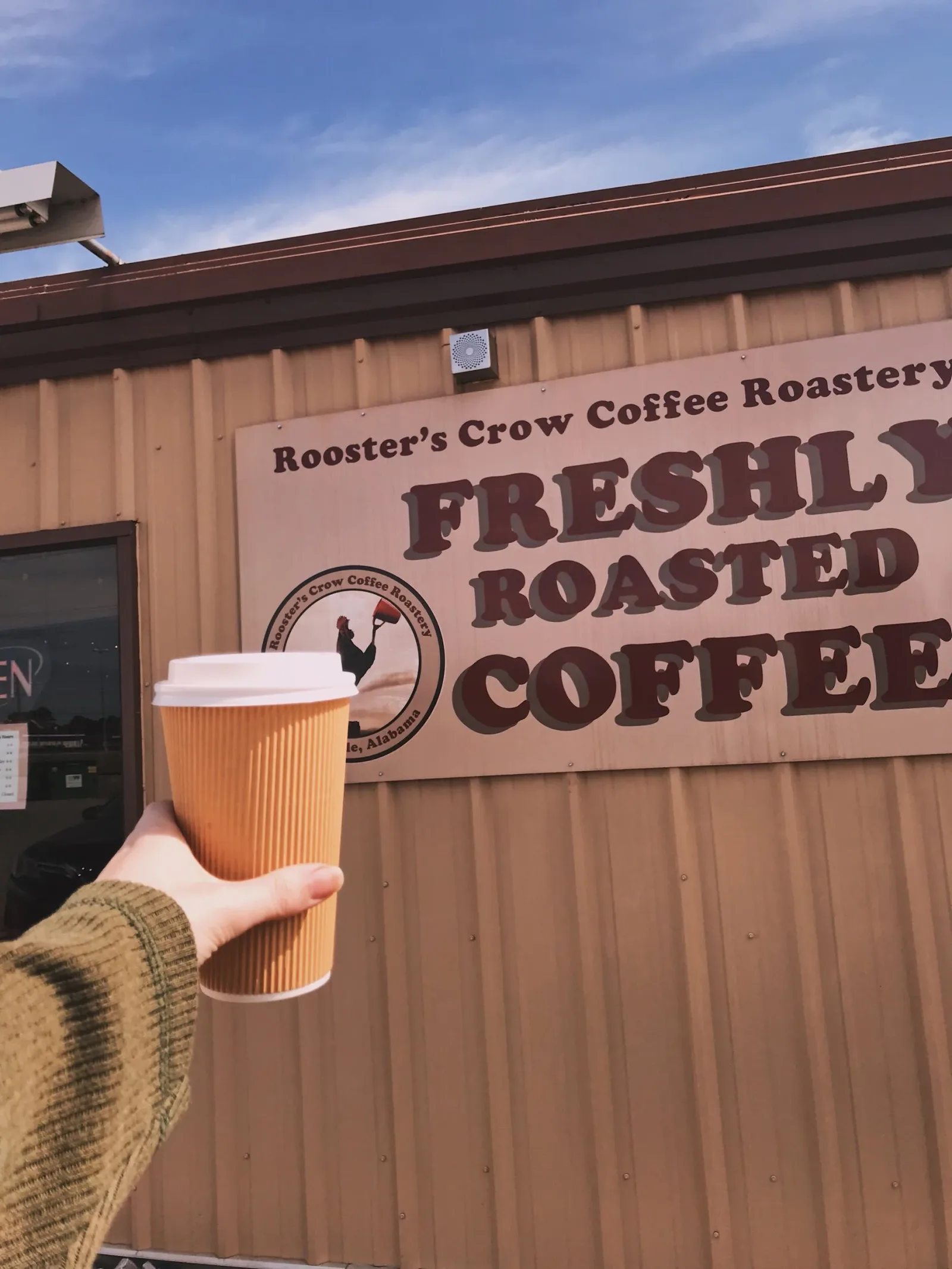 hand holding coffee cup at rooster's crow coffee roastery storefront., rooster's crow coffee roastery, alabama
