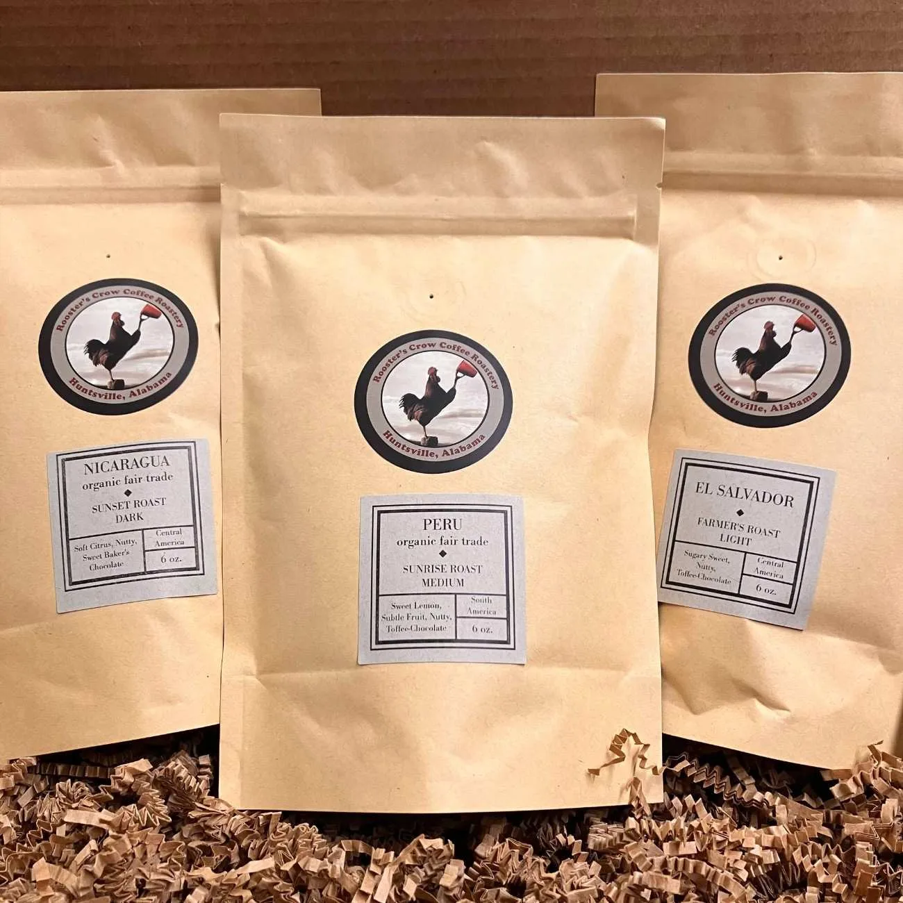 three kraft paper coffee bags with rooster logos displayed on brown background., rooster's crow coffee roastery, huntsville
