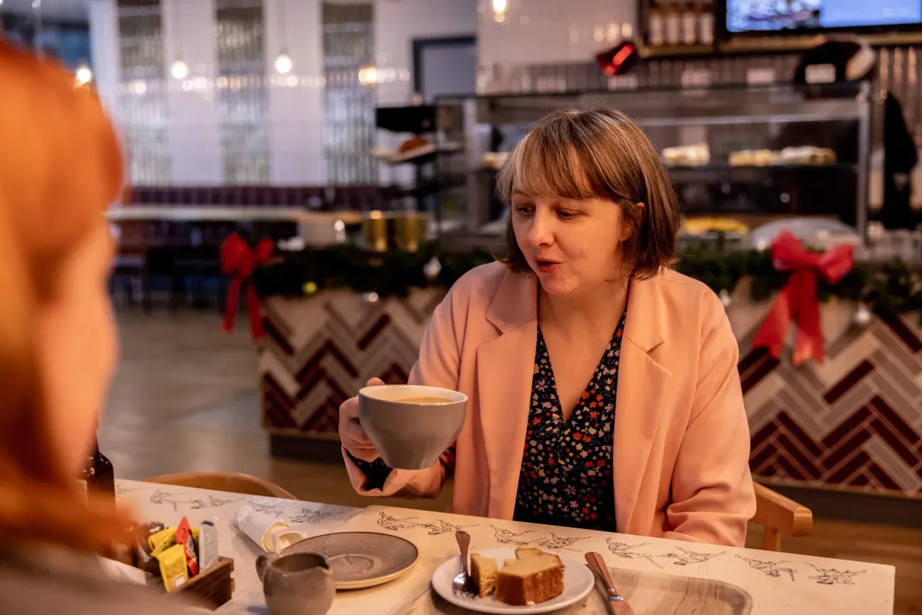 woman in peach blazer holding coffee cup at decorated holiday restaurant table., royal armouries museum, leeds