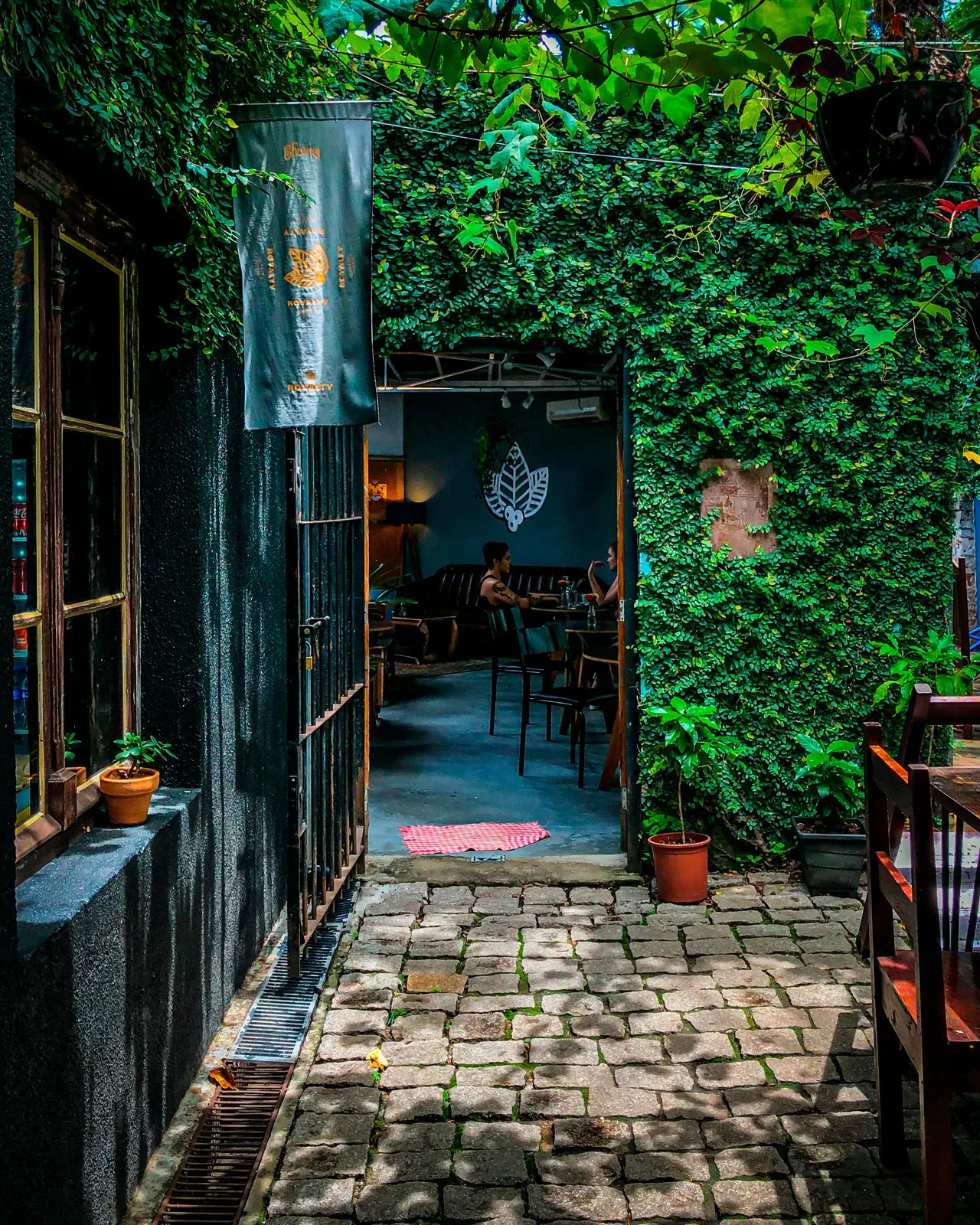 ivy-covered alleyway entrance to a cozy restaurant with leaf motif decor., royalty café, curitiba