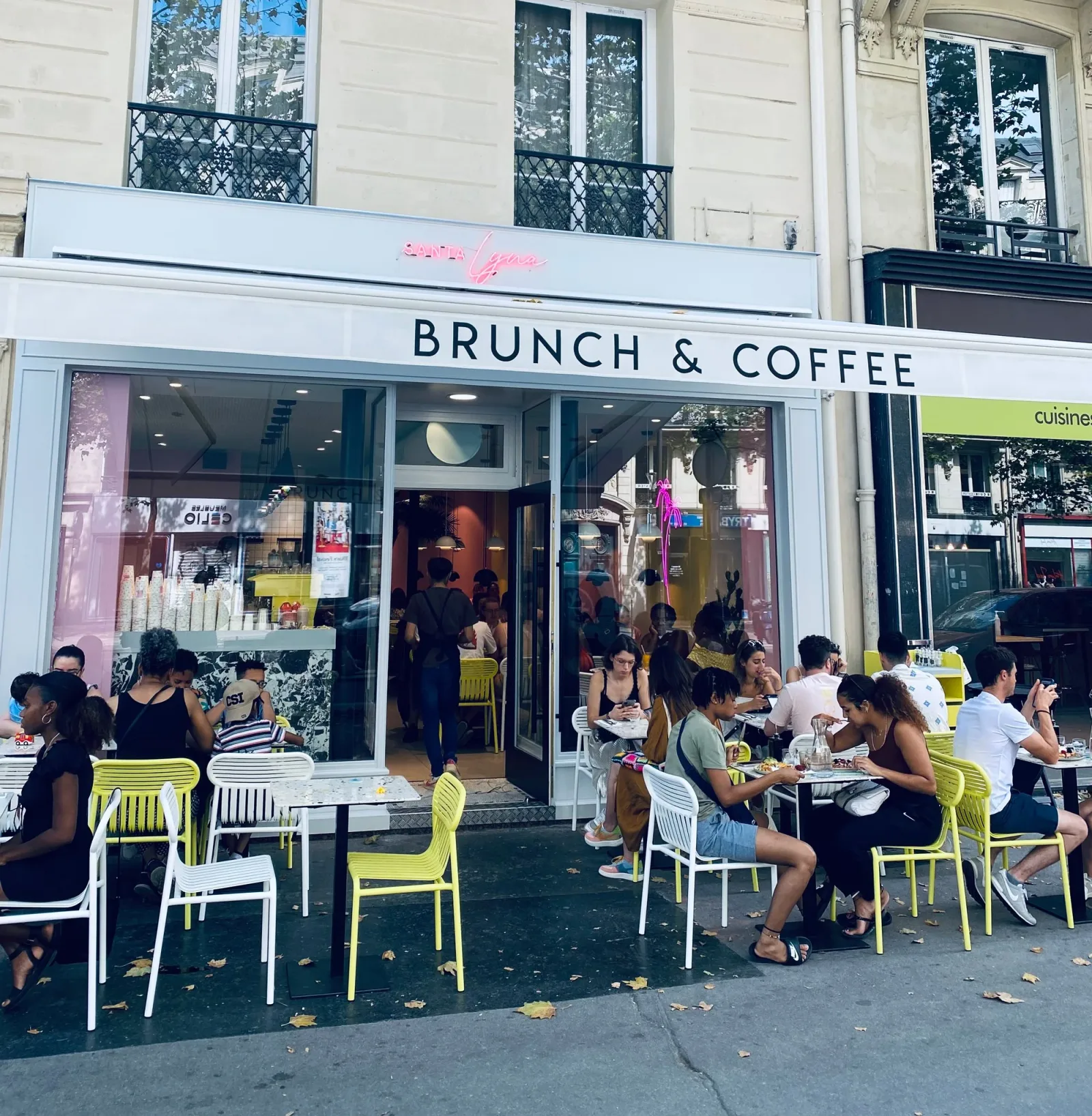 busy brunch café with yellow and white chairs on sidewalk seating., santa lyna, paris