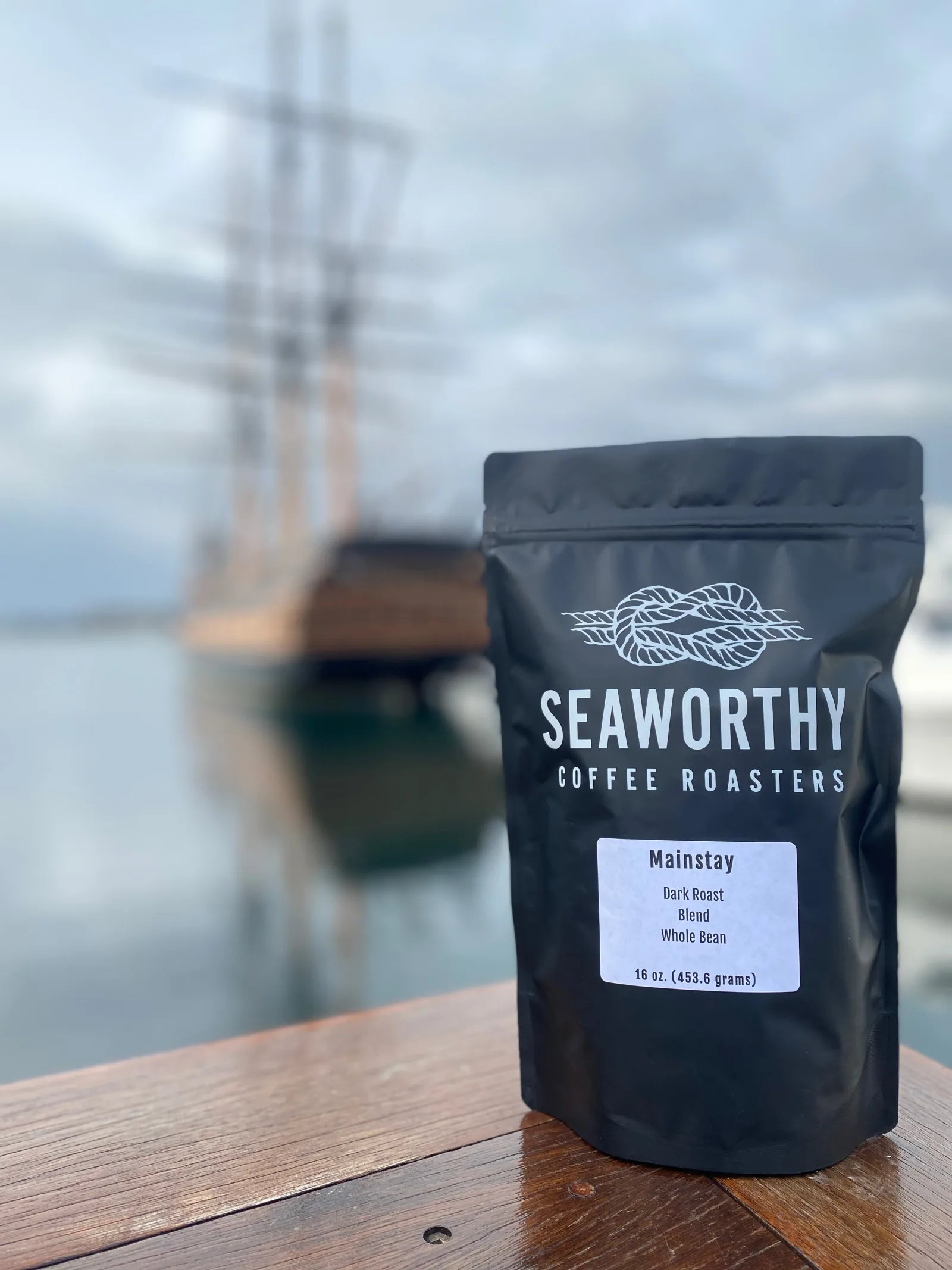 seaworthy coffee roasters package displayed on wooden dock with sailboat background., seaworthy coffee roasters, south kingst