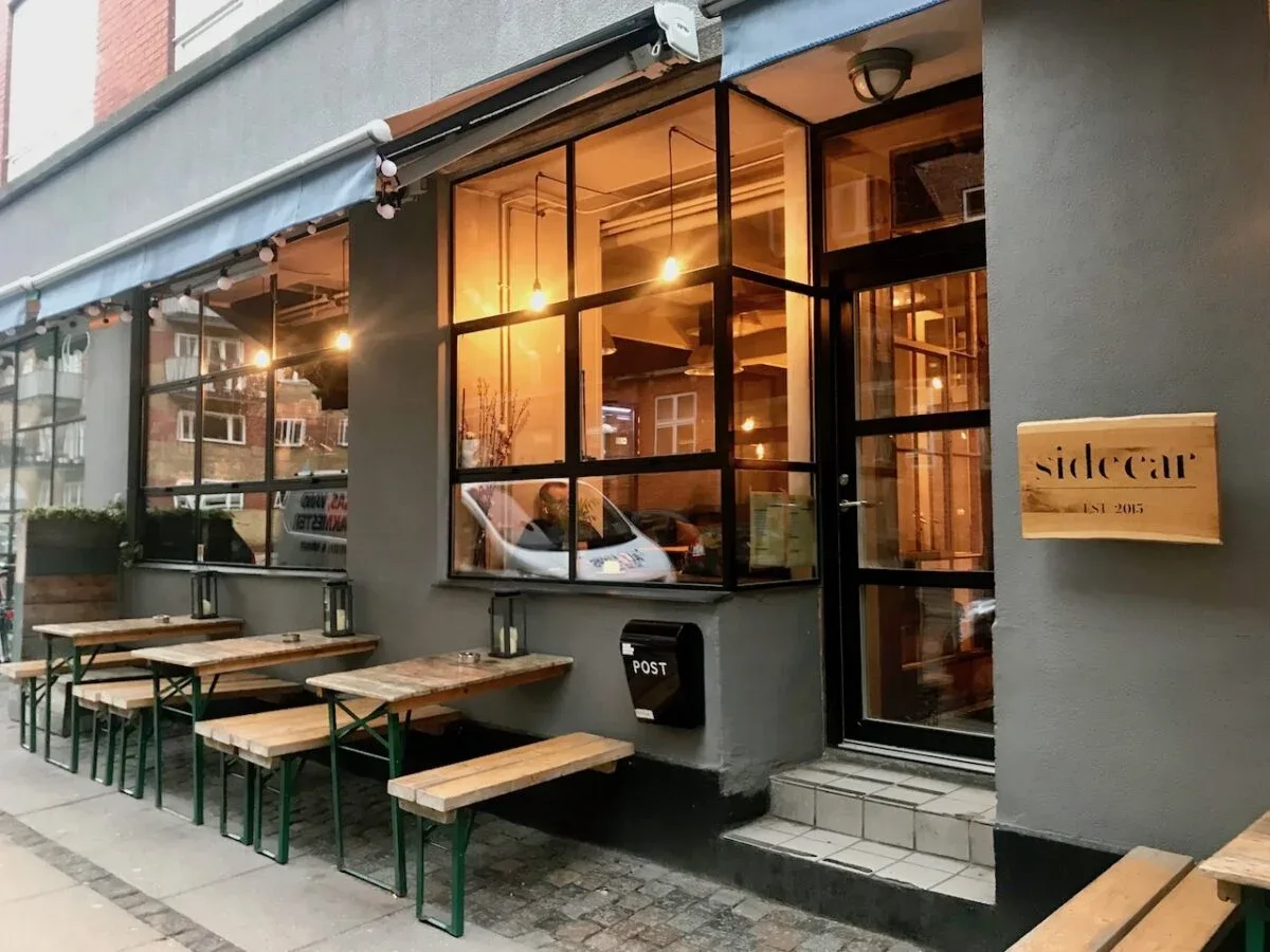 modern storefront with wooden benches, warm interior lighting, and "sidecar" signage., sidecar, copenhagen