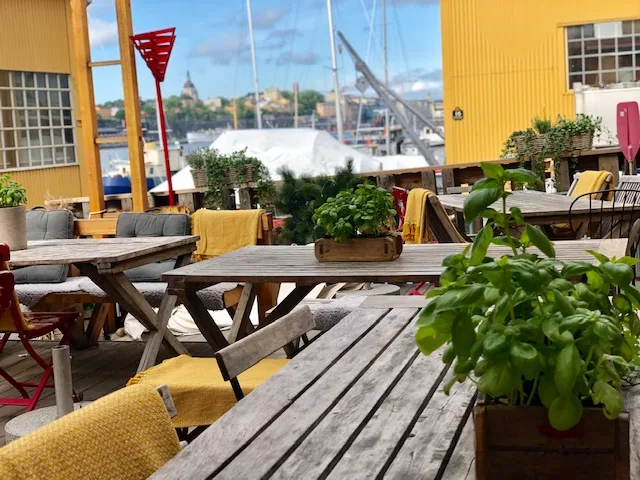 waterfront outdoor dining deck with yellow umbrellas and potted plants., skroten café & skeppshandel, stockholm