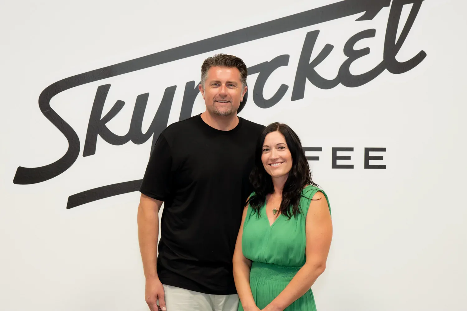 two people standing in front of a "skyrocket" branded wall sign., skyrocket coffee, austin