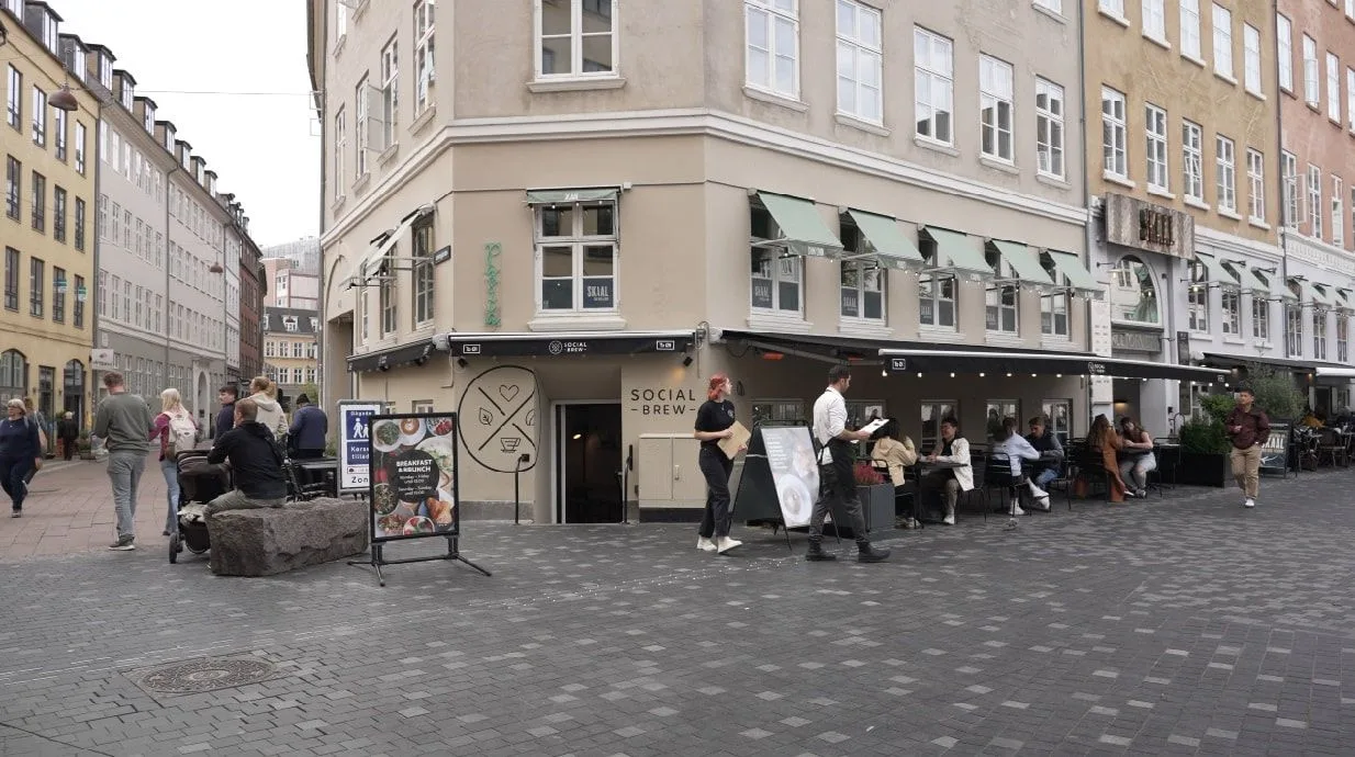 urban street plaza with social brew café, pedestrians, historic european architecture, and seating area., social brew, copenh