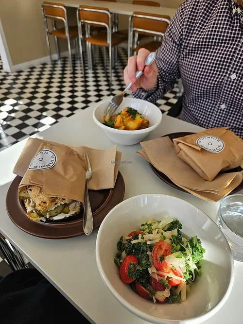 person eating salad at table with sandwiches in paper bags, checkered floor., sörkan rinkula, helsinki