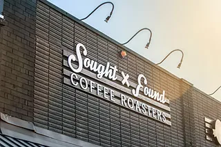 brick building storefront with "sought + found coffee roasters" illuminated white signage., sought and found coffee roasters,
