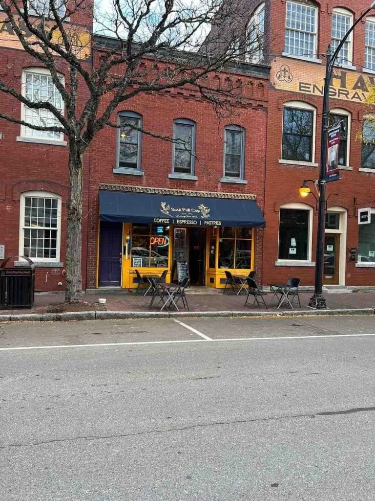 red brick building with coffee shop storefront, yellow trim, outdoor seating, bare tree., soul full cup coffeehouse, new york