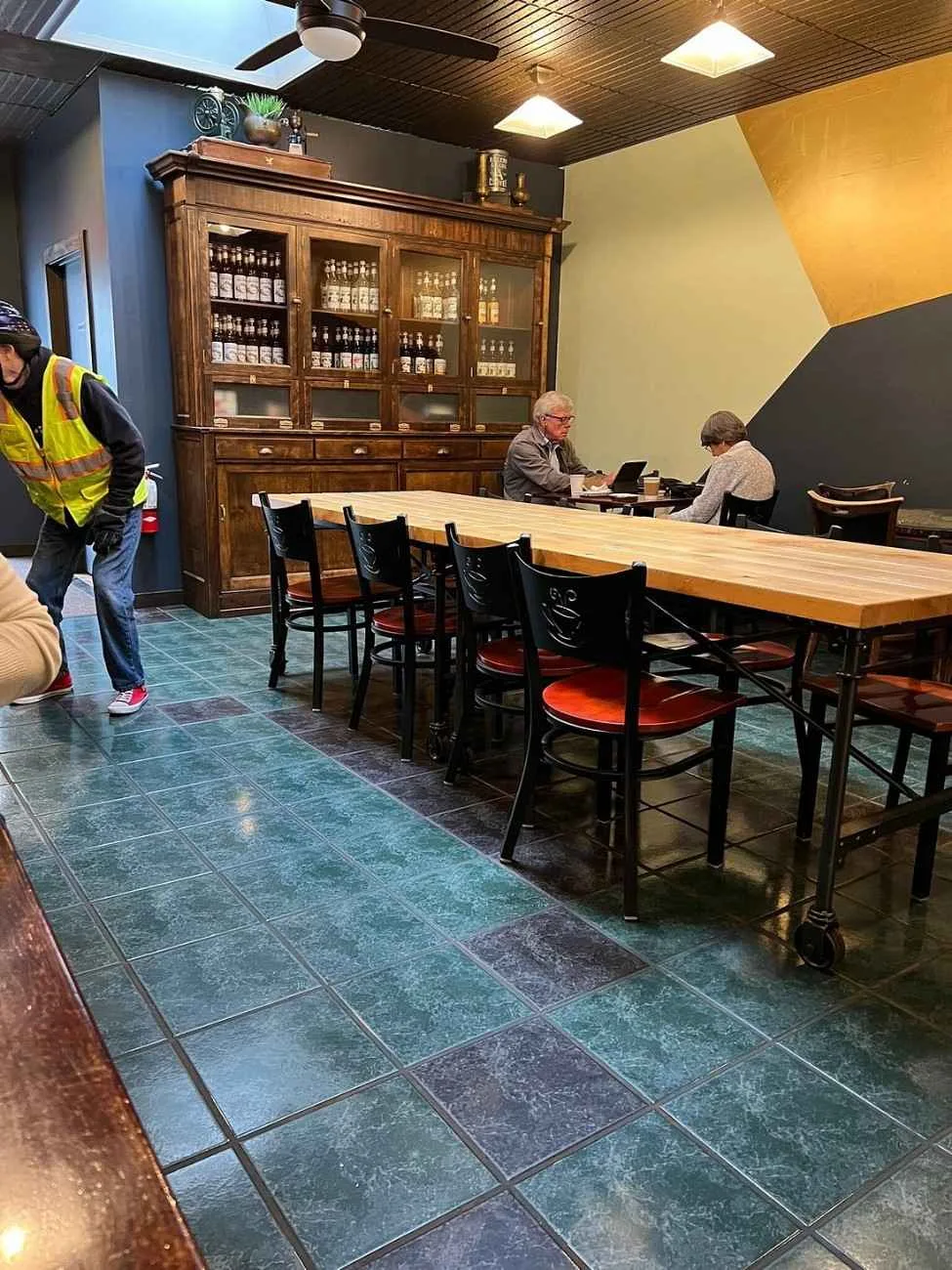 interior space with wooden cabinet, long table, seated workers, and visitor in safety vest., soul full cup coffeehouse, new y
