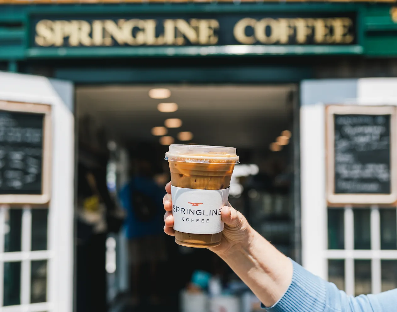 hand holding iced coffee cup in front of springline coffee storefront entrance., springline coffee, newport