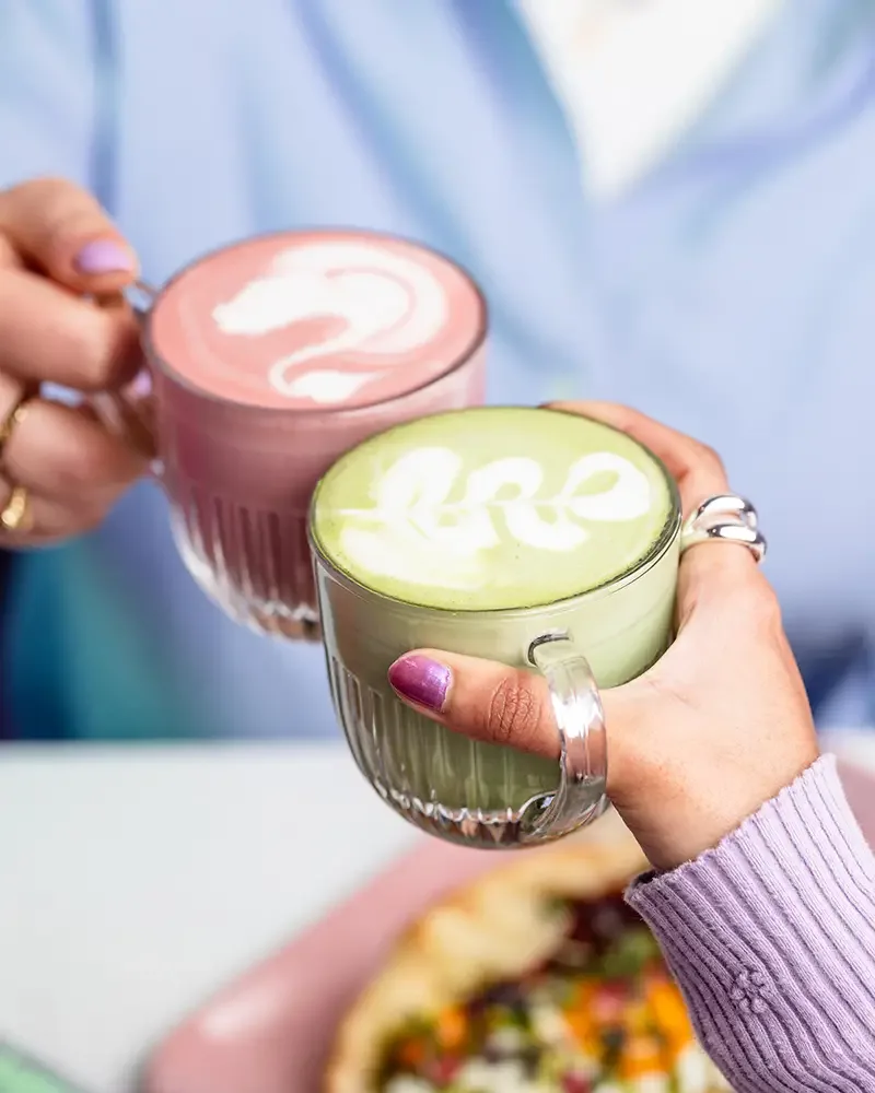 two specialty lattes with latte art held by person wearing rings outdoors., stella mia, paris