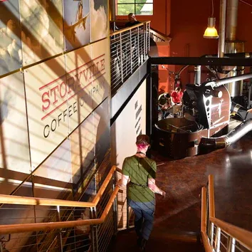 person in green jacket descending stairs in rustic coffee shop interior., storyville coffee company, bremerton