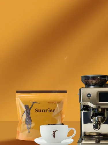 yellow coffee bag, white cup with figure, espresso machine on orange background., storyville coffee company, bremerton