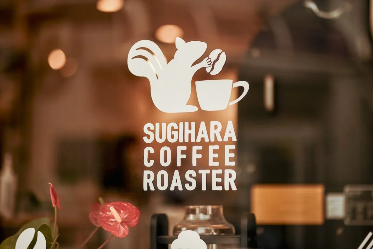 sugihara coffee roaster logo displayed on window with blurred cafe interior and pink flower., sugihara coffee roaster, osaka